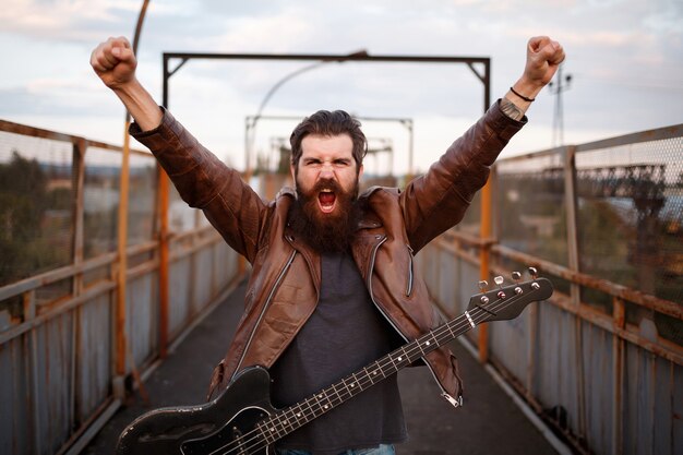 brutal bearded man a guitarist with a mustache in a brown leather jacket raised his hands and shouts with a guitar