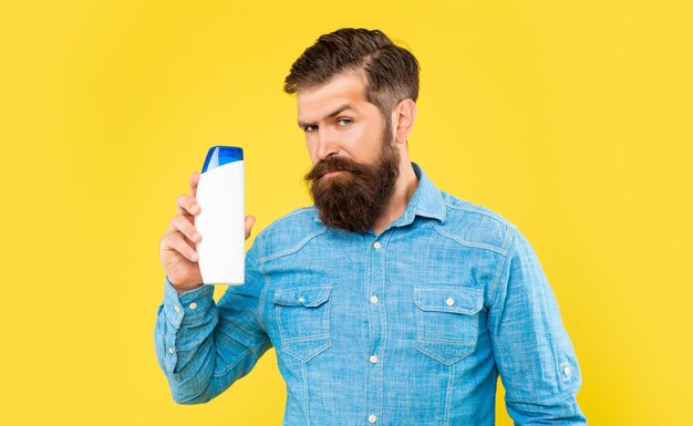 Brutal bearded man hold shampoo bottle on yellow background skincare