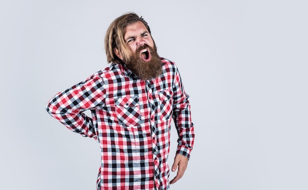 Жестокий бородатый мужчина в клетчатой рубашке с пышной бородой и усами чувствует боль в спине