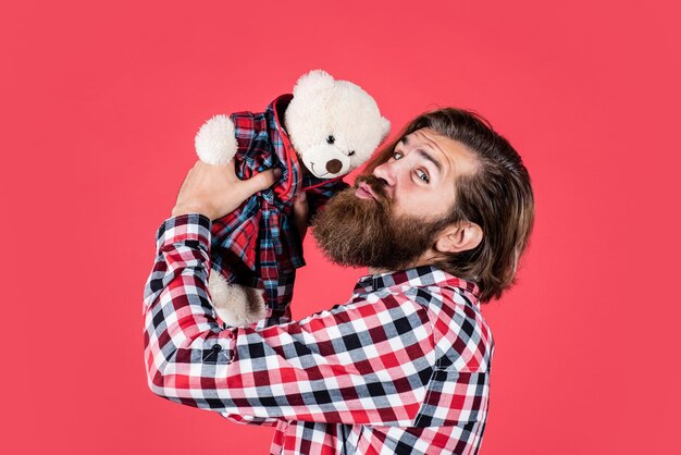 Brutal bearded man wear checkered shirt having lush beard and moustache kiss teddy bear toy love
