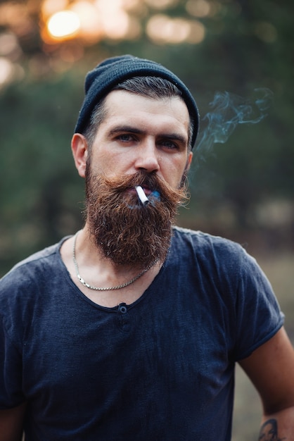 Photo a brutal bearded man with a long beard and mustache in a tshirt and a warm hat on his shoulder