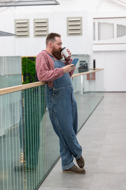 Brutale barbuto lavoratore autonomo bere caffè, utilizza lo smartphone. è ora di fare una pausa. una pausa durante il lavoro