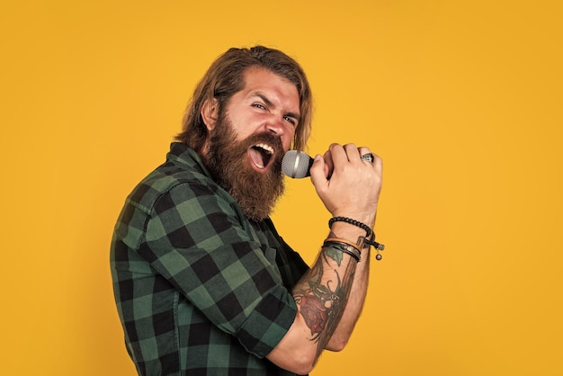 Brutal caucasian hipster with beard in shirt sing in karaoke microphone