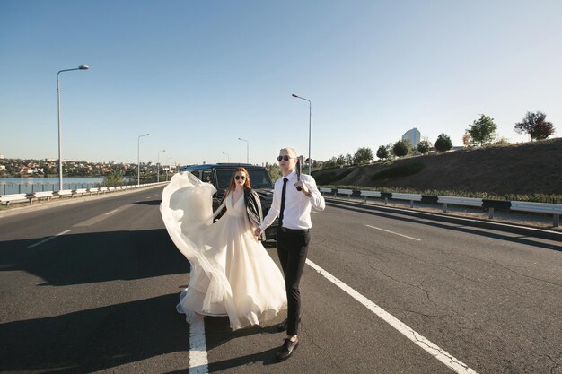 Brutal couple the bride and groom with a bat in leather jackets near the car on the road