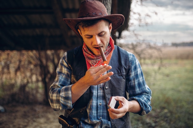 Brutal cowboy lights a cigar with matches