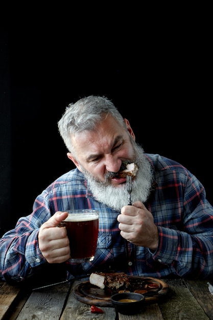 Brutal gray-haired adult man crazy about mustard steak and beer