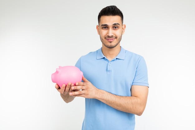 Brutal man in a blue shirt holds a piggy bank on a white with copy space