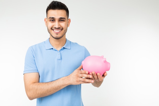 Brutal man in a blue T-shirt holds a piggy bank on a white background