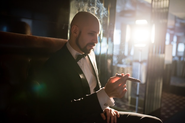 A brutal man in a dress coat smokes a cigar.