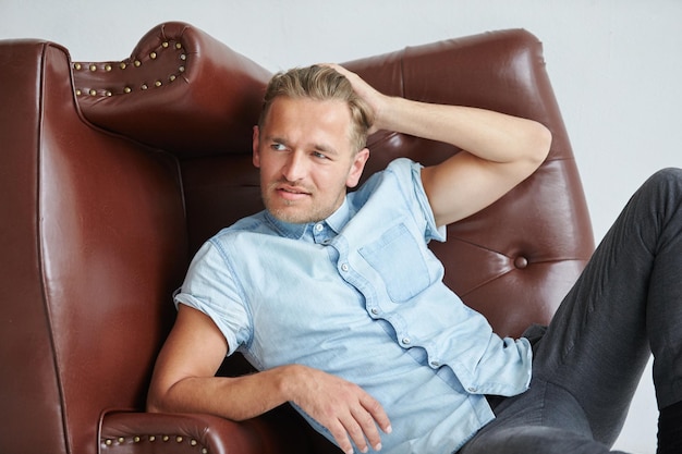 Brutal man in a shirt with short sleeves sitting in the chair his fists clenched slightly bent under