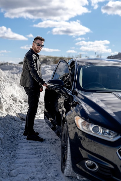 Brutal man standing on the road near car Man is going to sit in the luxury auto