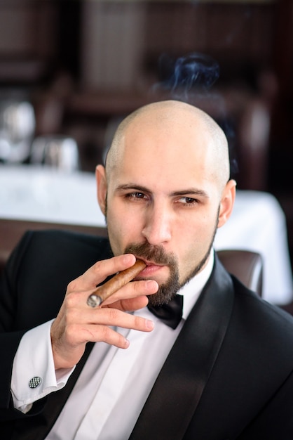 A brutal man in a suit smokes a cigar.