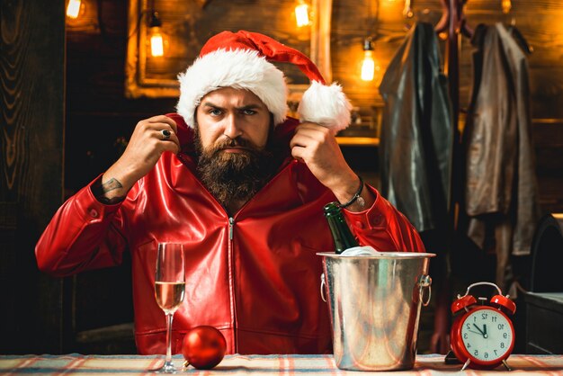 Brutal masculine bearded Santa man with clock and champagne getting resdy to meet New Year