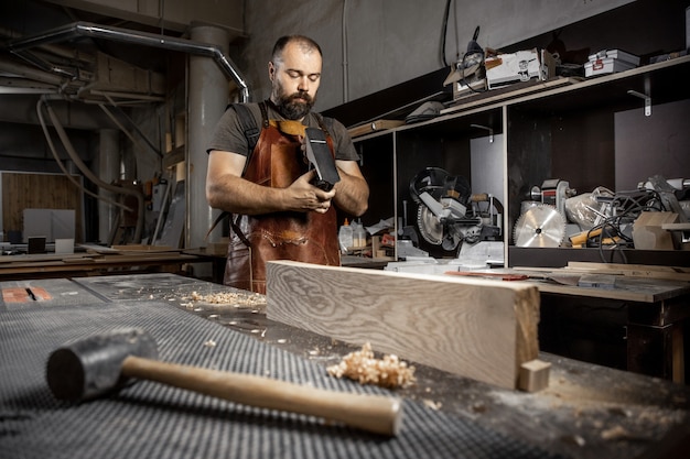 Brutal master carpenter in an apron adjusts plane in workshop