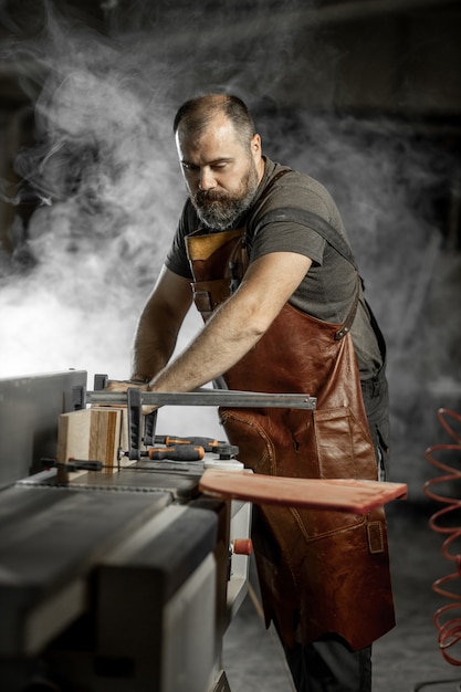 Brutal master carpenter saws wood blanks on machine in workshop