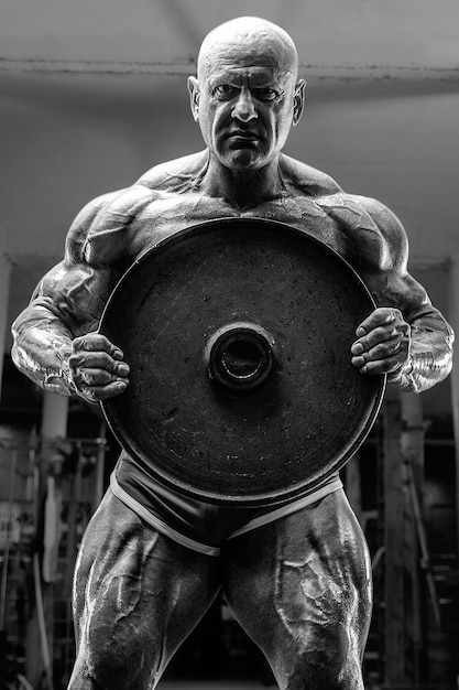 Brutal and muscular strong bodybuilder athletic man pumping up\
muscles at workout in the gym