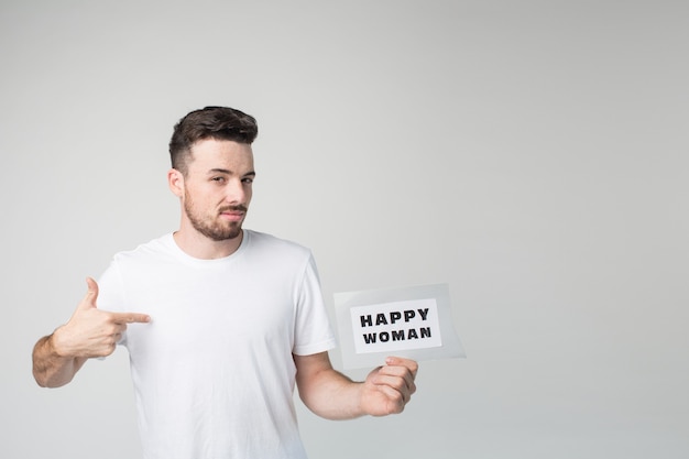 Brutal serious self-confident guy posing on camera and pointing on himself. Hold piece of paper with happy woman sign.