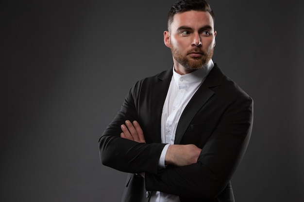 brutal unshaven businessman, dressed in a black suit and white shirt, posing against a dark background.