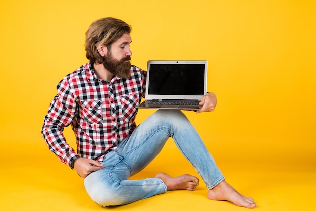 Brutale bebaarde man draagt geruit hemd met weelderige baard en snor die op laptop werkt, nieuwe technologie.