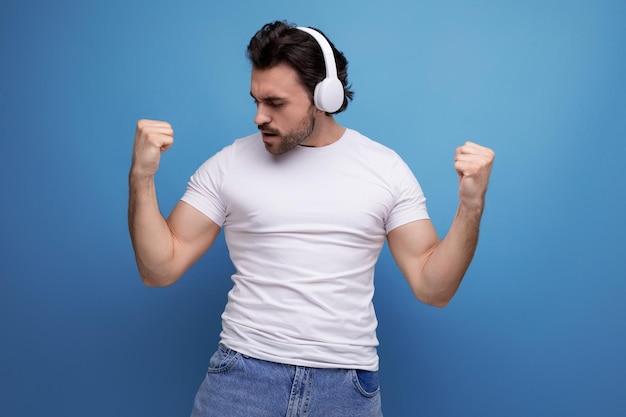 Brutale brunette man in een wit t-shirt luistert naar muziek op een koptelefoon