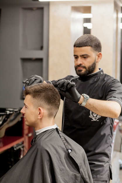 Brutale kerel in moderne kapperszaak. Kapper maakt kapsel een man. Hoofdkapper doet kapsel met haartrimmer. kapperszaak