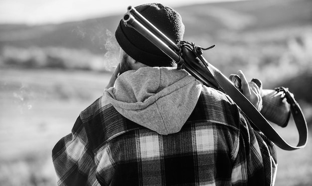 Brutality and masculinity hunter carry rifle gun on shoulder\
rear view guy hunter spend leisure hunting hunting masculine hobby\
leisure concept man brutal guy gamekeeper in hat nature\
background