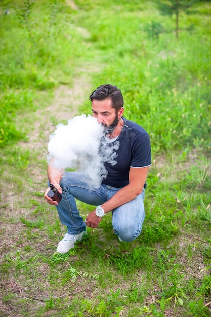 Photo brutalvape man smoking an electronic cigarette in a forest clearing. the new technology cigarette.