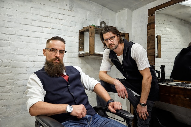 Brute man in de moderne Barber Shop. Kapper maakt van kapsel een man met een lange baard. Kapper doet kapsel met een schaar en kam