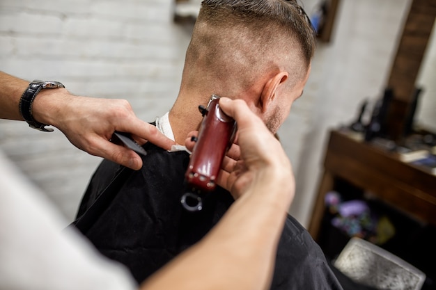 Brute man in de moderne Barber Shop. Kapper maakt van kapsel een man met een lange baard. Meester kapper doet kapsel met een tondeuse