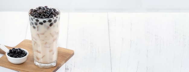 Bubble milk tea with tapioca pearl topping, famous Taiwanese drink on white wooden table background in drinking glass, close up, copy space