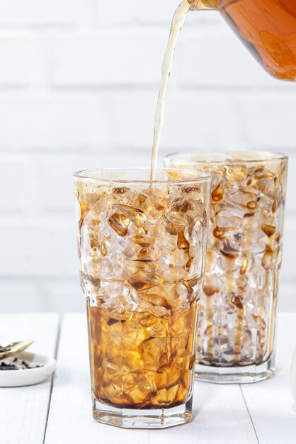 Bubble tea maken gieten van melkthee in bruine suikerpatroon drinkglas beker op witte houten tafel achtergrond close-up kopie ruimte