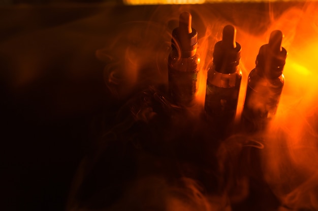 Bubbles liquid bottles on a dark background with smoke and orange light. vape background.