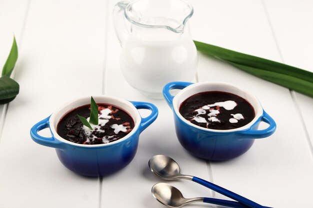 Bubur Ketan Hitam of zwarte kleefrijstpap, is een traditioneel Indonesisch dessert geserveerd met kokosmelksaus en gegarneerd met pandanbladeren. Twee Kom, Witte Achtergrond, Close-up