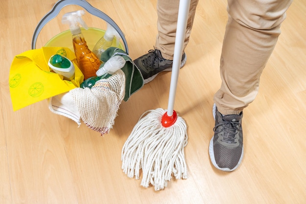 Bucket of cleaning supplies next to the legs of a man holding a rope mop.