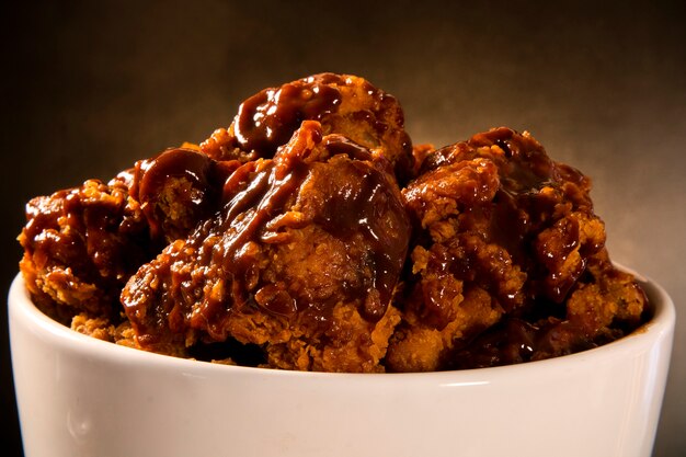 Bucket full of crispy kentucky fried chicken with smoke and barbecue sauce on brown background. Selective focus.