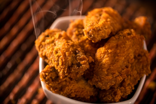 Bucket full of crispy kentucky fried chicken with smoke on brown background. Selective focus.