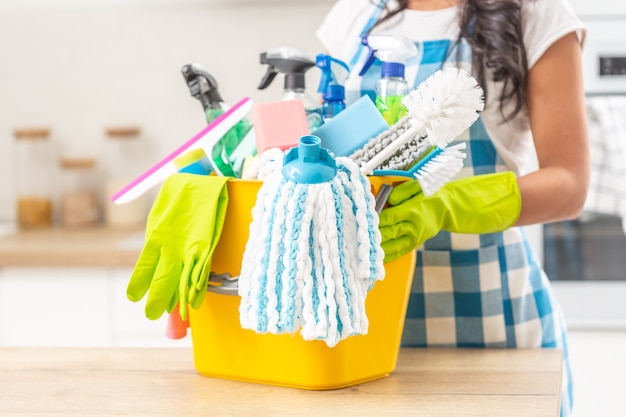 Bucket full of house clenaing stuff on a kitchen desk with a female holding it in rubber gloves.