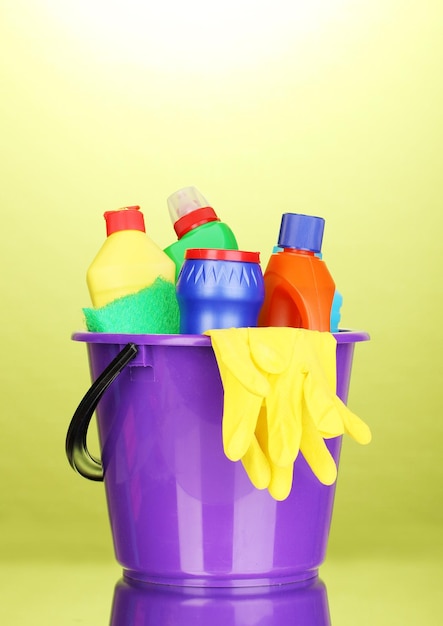 Bucket with cleaning items on green background