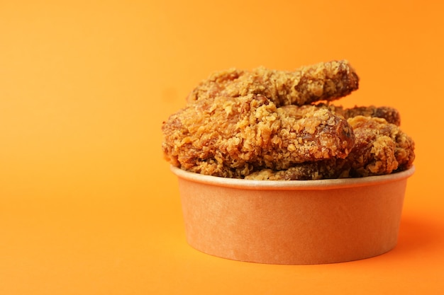 Bucket with fried chicken on orange background