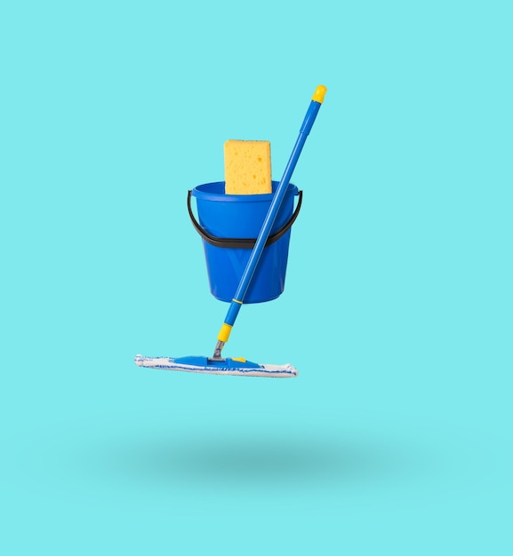 Photo a bucket with a large sponge and a mop levitating on a light background the concept of cleaning the premises