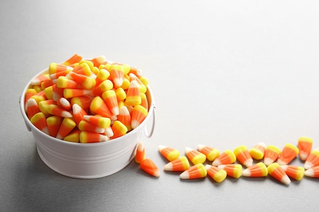 Bucket with tasty halloween candies on light background