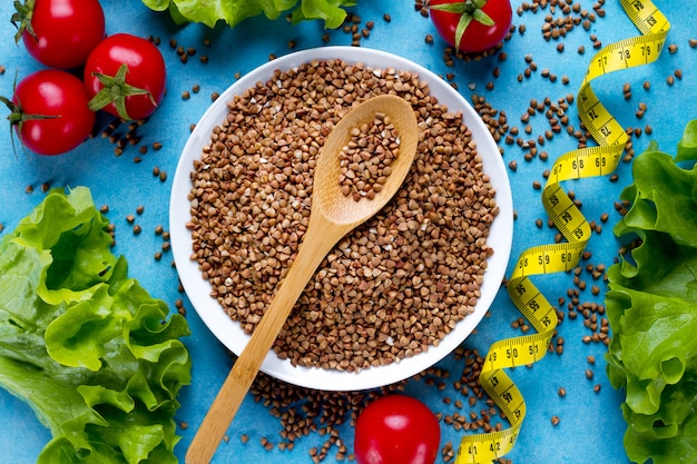 Buckwheat bowl and spoon with fresh ripe vegetables and yellow measuring tape