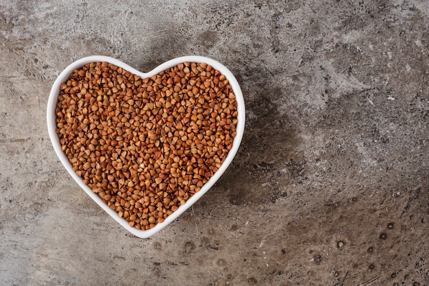 Grano saraceno in una tazza-cuore su uno sfondo di cemento