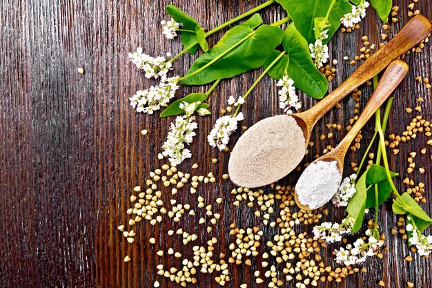 Buckwheat flour from brown and green cereals in spoons, flowers