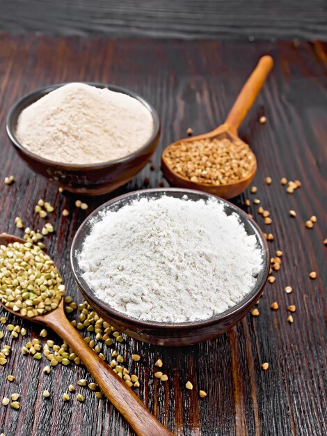 Buckwheat flour from green and brown cereals in two bowls, groats in spoons and on the table against the background of a dark wooden board