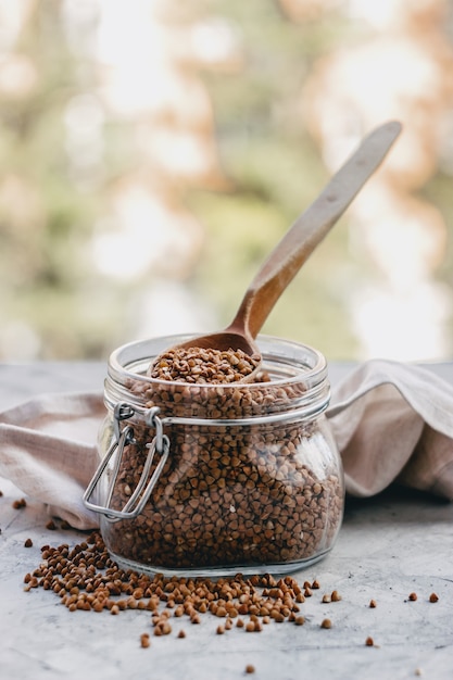 buckwheat in a glass jar with a wooden spoon, on a gray light surface