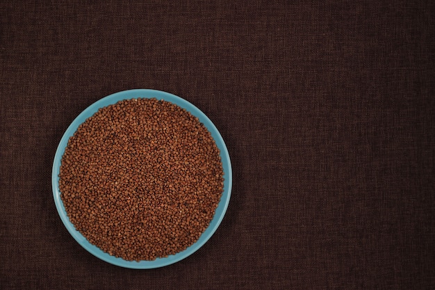 Buckwheat groats in a blue bowl and brown linen background with copy space for recipe
