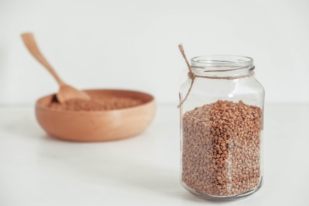 Buckwheat kernels in a glass jar wooden bowl and spoon on white background