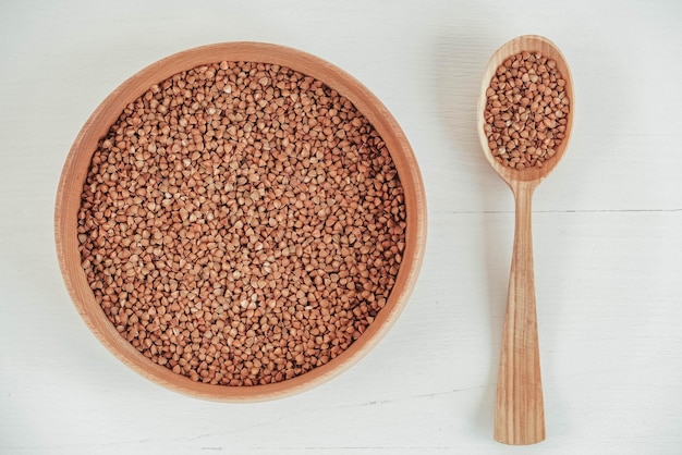 Buckwheat kernels in wooden bowl and spoon on white background. Top view. Copy, empty space for text