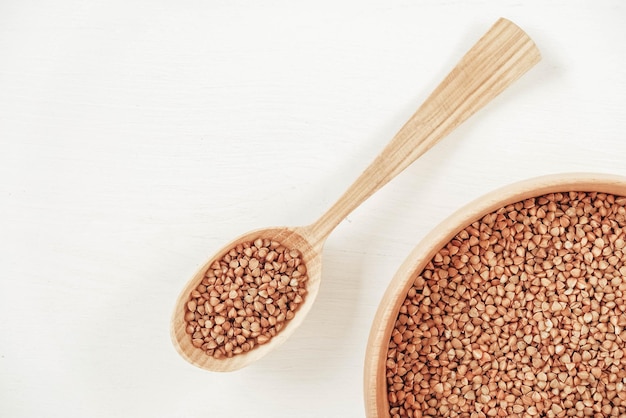 Buckwheat kernels in wooden bowl and spoon on white background. Top view. Copy, empty space for text